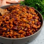 Crock pot baked beans in a grey bowl with a wooden spoon in it.