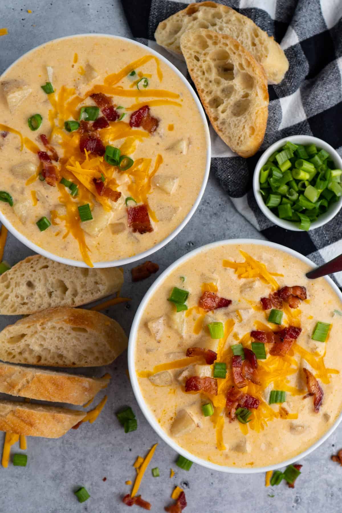 Two bowls of Crock Potato potato soup garnished with bacon, cheese, and green onions.