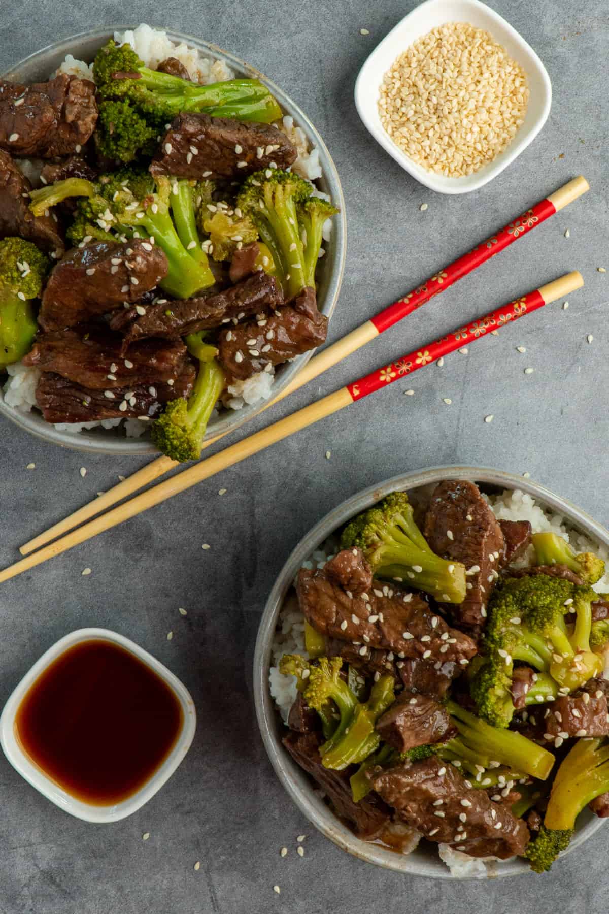 Over head look at two bowls of beef and broccoli with chop sticks in the middle.