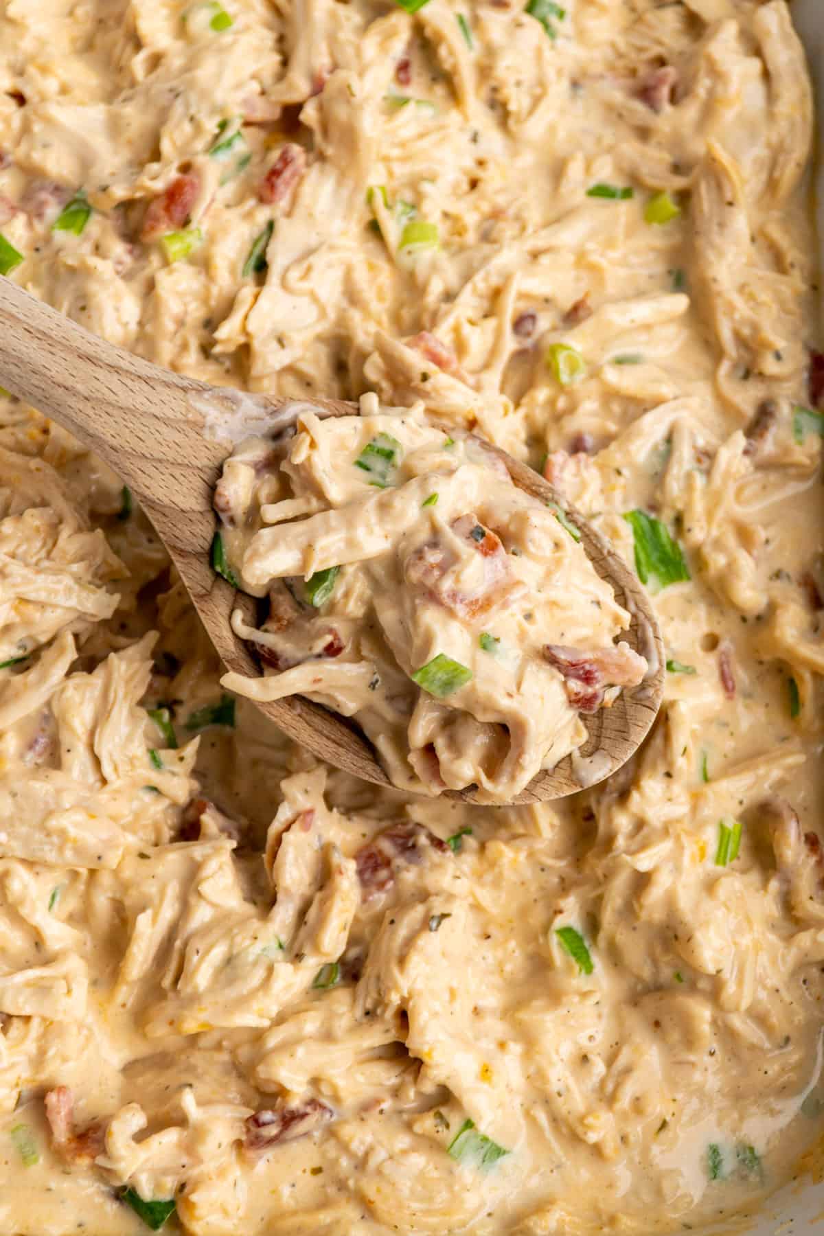 Close up of creamy ranch chicken on a wooden spoon over a slow cooker.