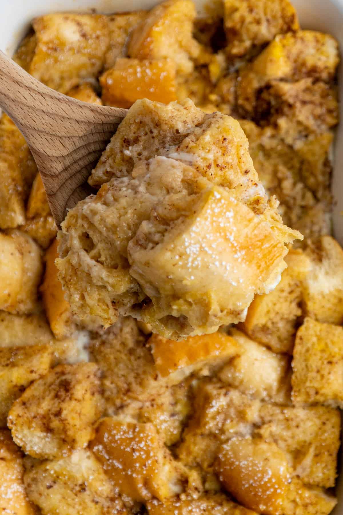 Scoop of French toast on a wooden spoon over a slow cooker.