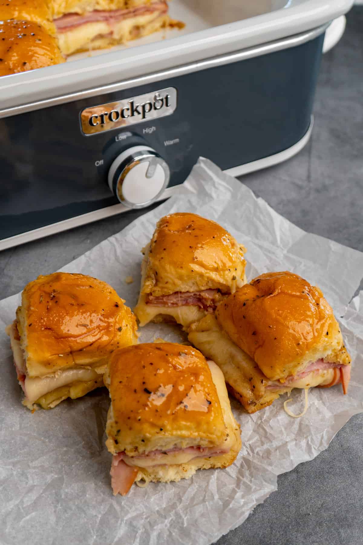 Ham and cheese sliders on parchment paper in front of a Crock-Pot.