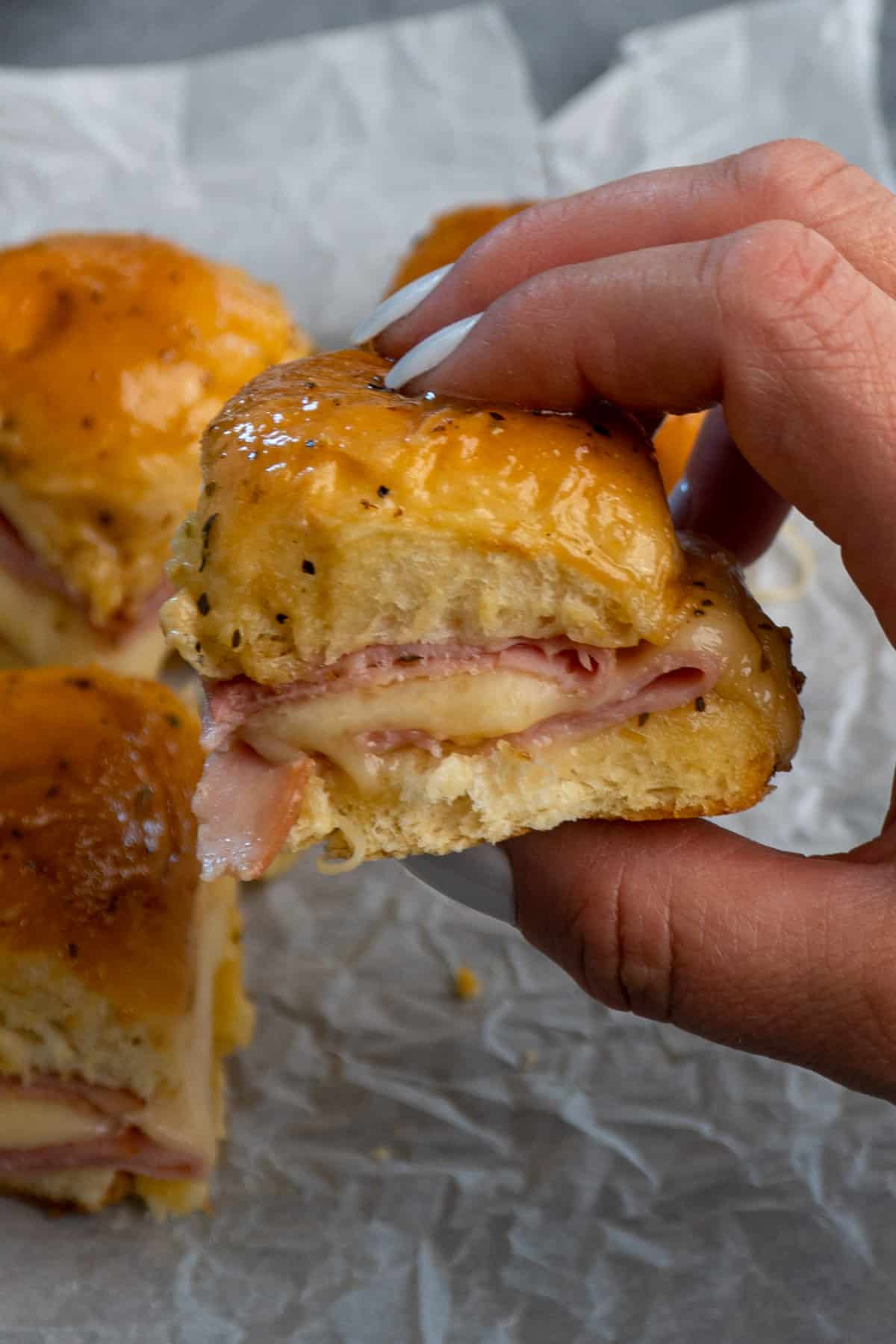 Close up of a hand holding a ham and cheese slider.