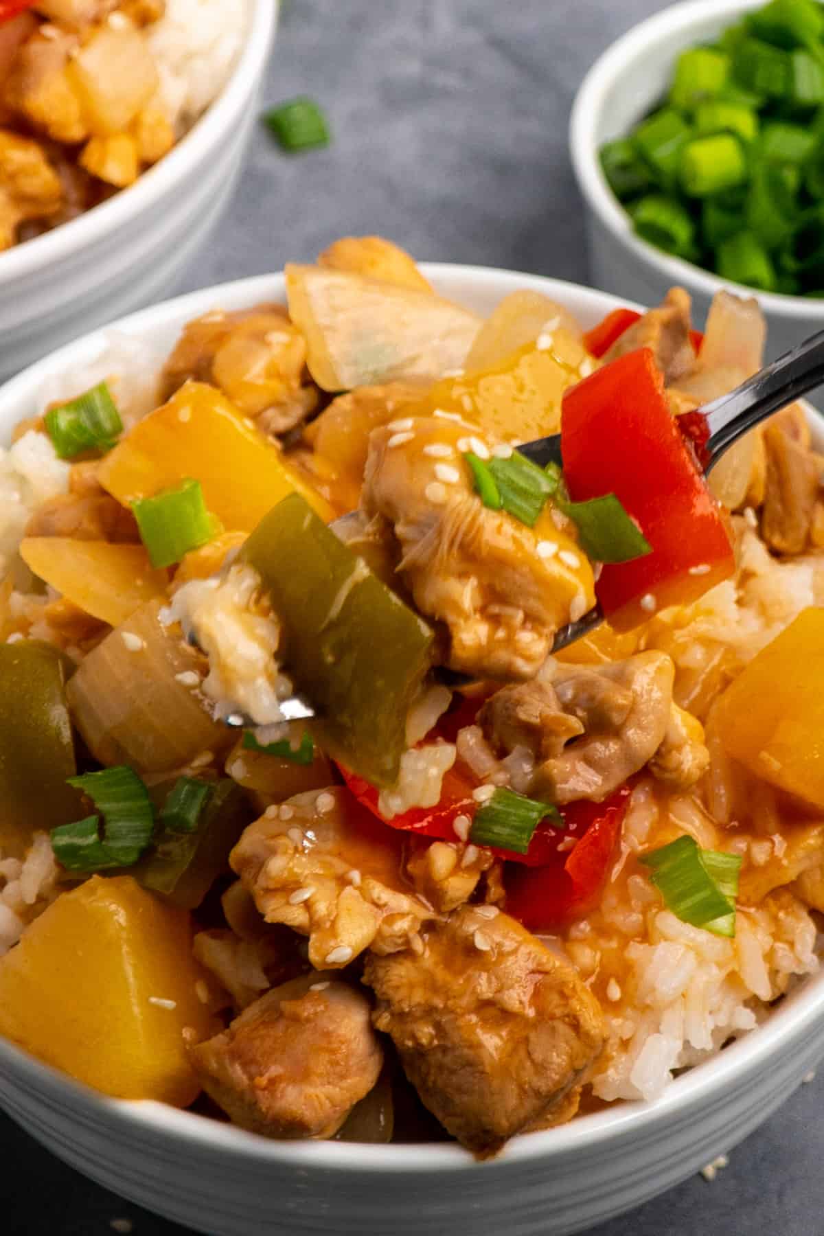 Close up of Crock-Pot Hawaiian chicken on a fork over a bowl of rice.