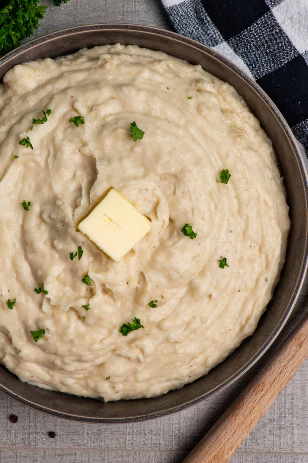 Close up of Crock-Pot mashed potatoes in a grey bowl garnished with fresh parley and butter.
