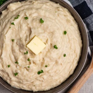 Close up of Crock-Pot mashed potatoes in a grey bowl garnished with fresh parley and butter.