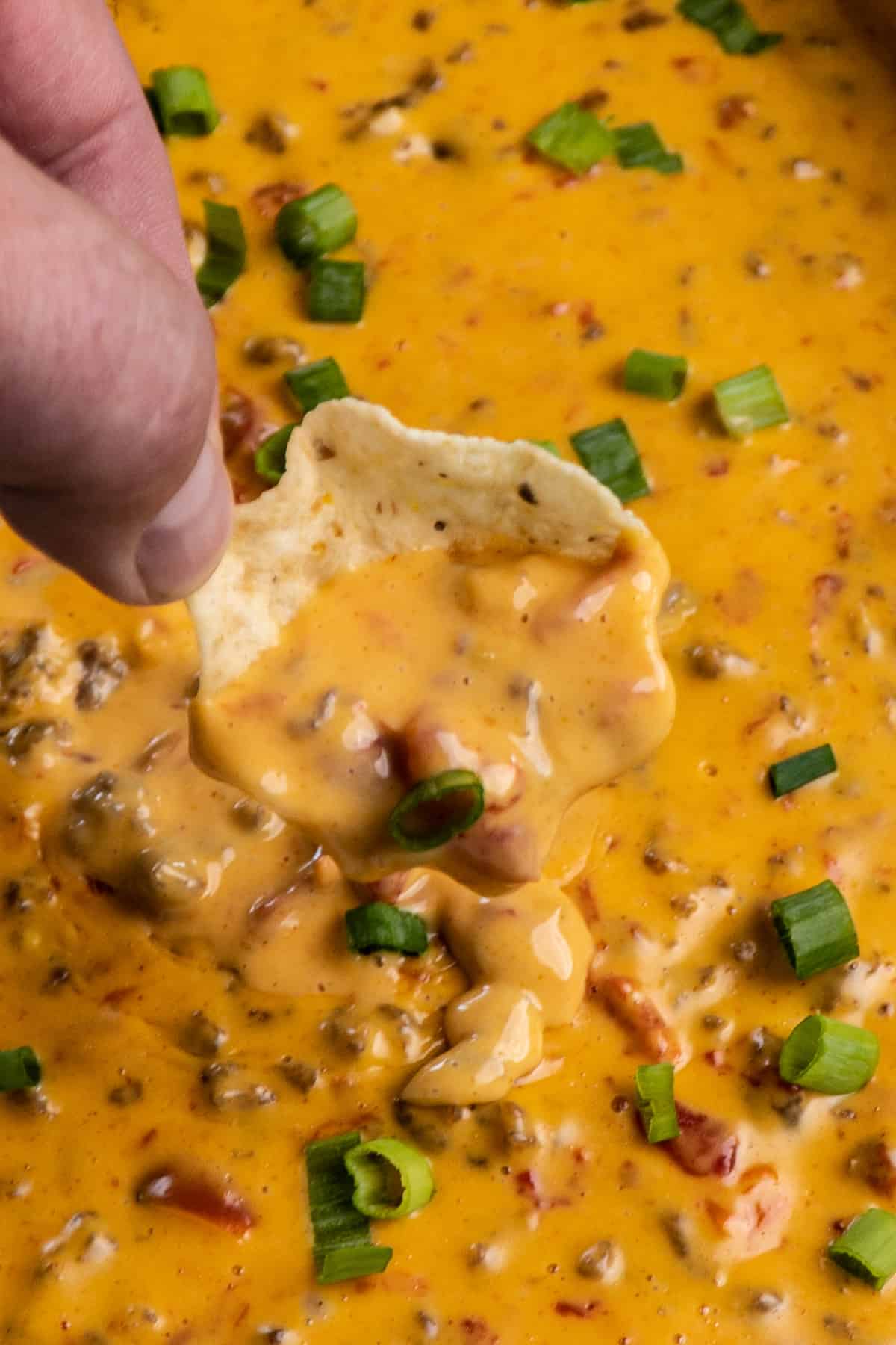 Close up of rotel dip on a tortilla chip being held over a crock pot.