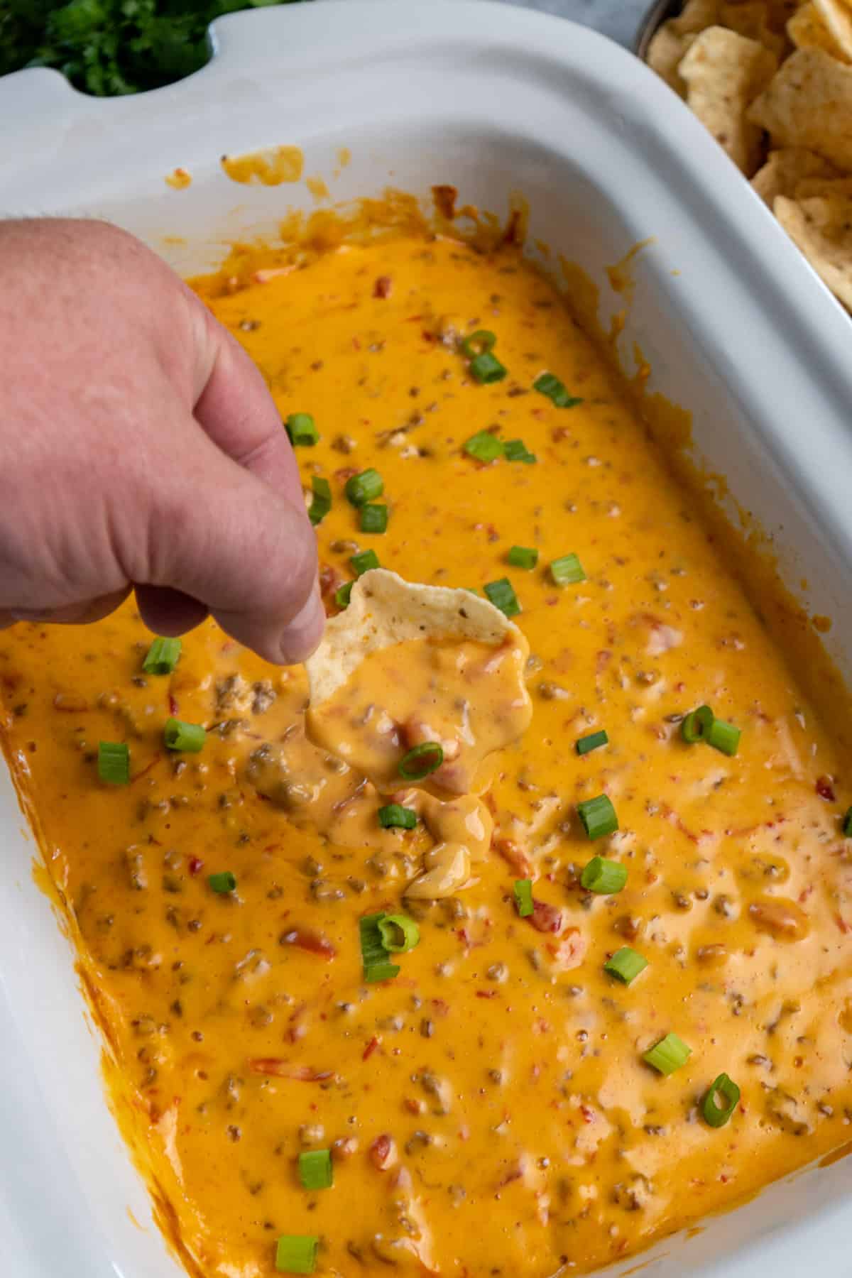 Rotel dip on a tortilla chip being held over a crock pot.