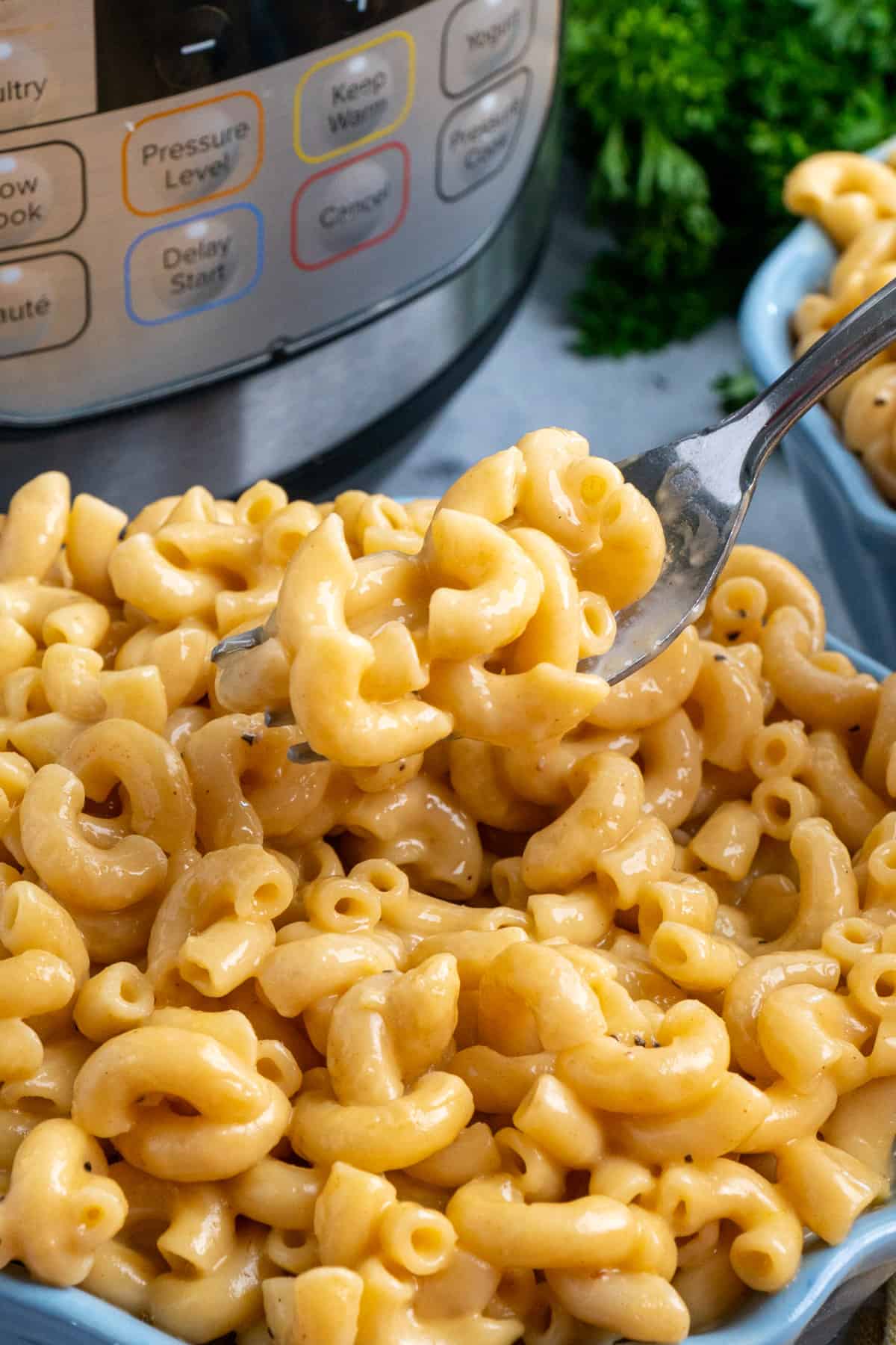 Close up of Instant Pot mac and cheese on a fork over a bowl of macaroni.