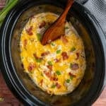Crack chicken in a slow cooker with a wooden spoon ready to be served.