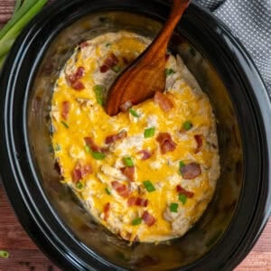 Crack chicken in a slow cooker with a wooden spoon ready to be served.