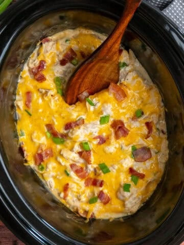 Crack chicken in a slow cooker with a wooden spoon ready to be served.