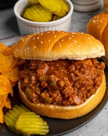 Close up of slow cooker sloppy joe's on a bun served with chips and pickles.