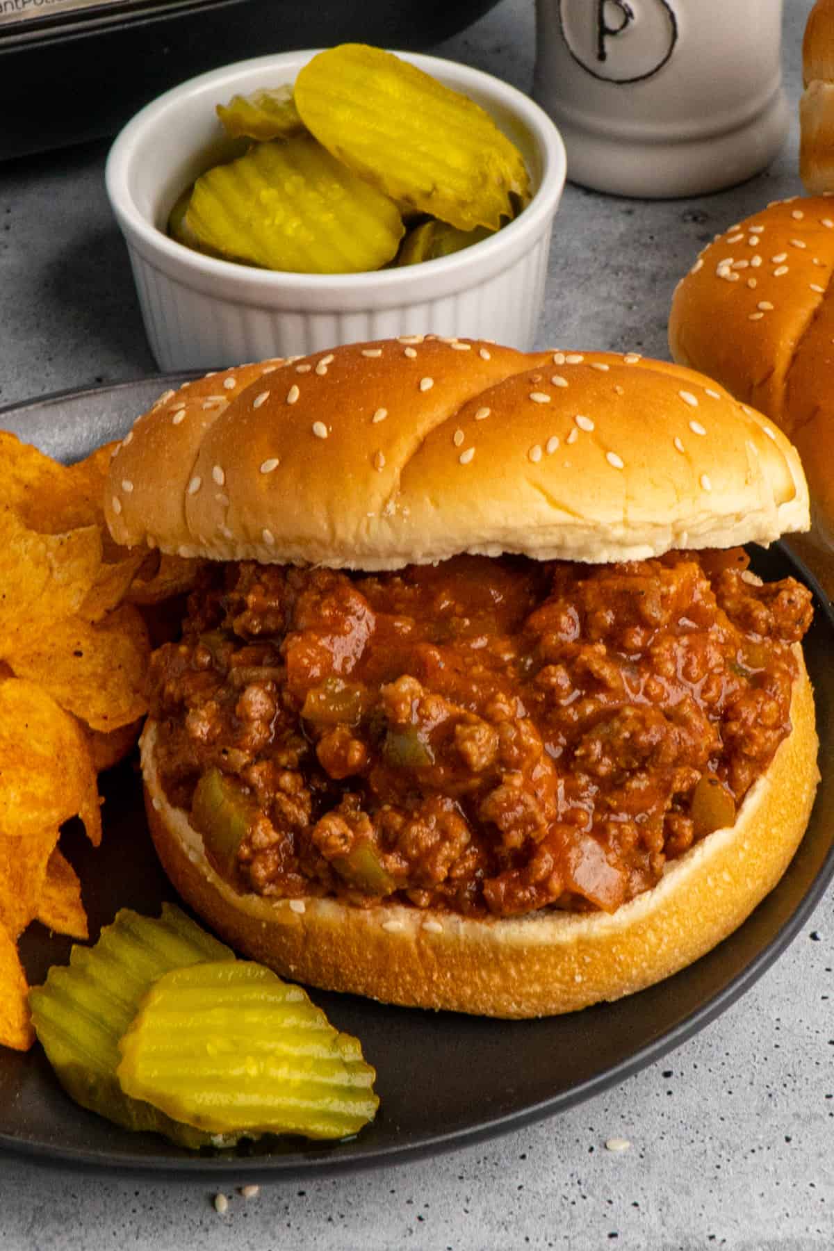 Close up of slow cooker sloppy joes on a bun served with chips and pickles.