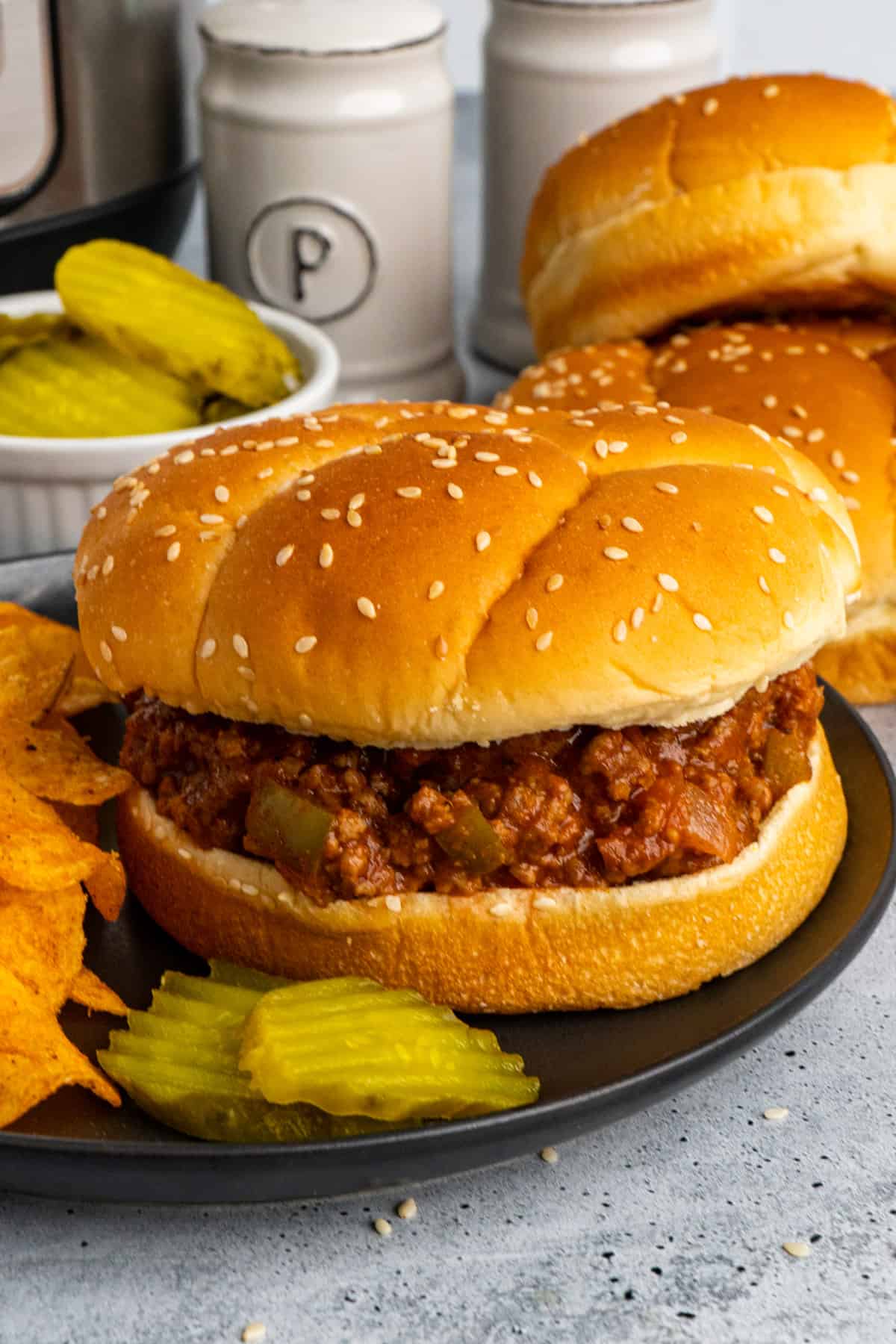 Close up of slow cooker sloppy joes on a bun served with chips and pickles.