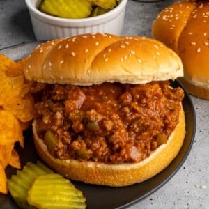 Close up of slow cooker sloppy joe's on a bun served with chips and pickles.