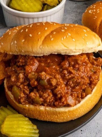 Crockpot sloppy joes on a bun served with chips and pickles.