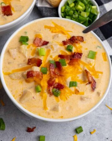 Close up of Crock-Pot baked potato soup in a white bowl with cheese and bacon on top.