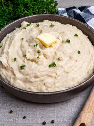 Close up of Crock-Pot mashed potatoes in a grey bowl garnished with butter.