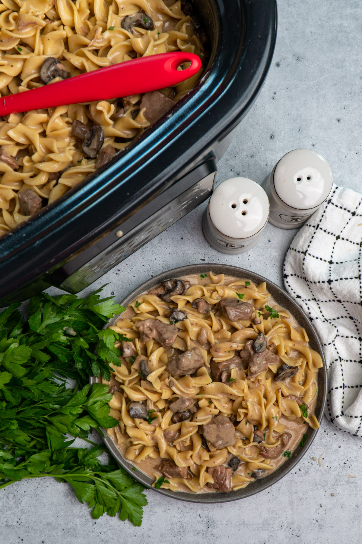 Overhead look at Crock-Pot beef stroganoff on a grey plate with a parsley garnish to the side.