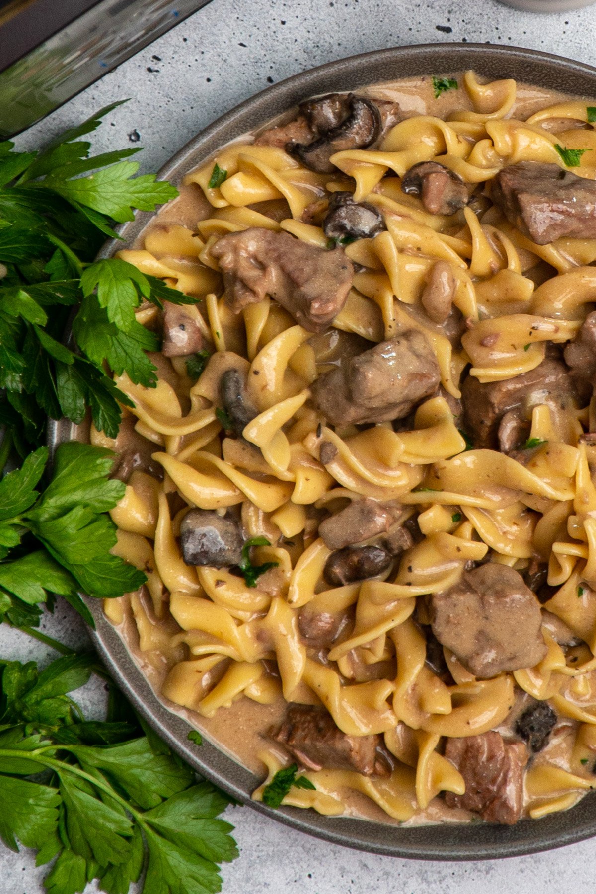 Close up of Crock-pot beef stroganoff on a grey plate garnished with parsley.