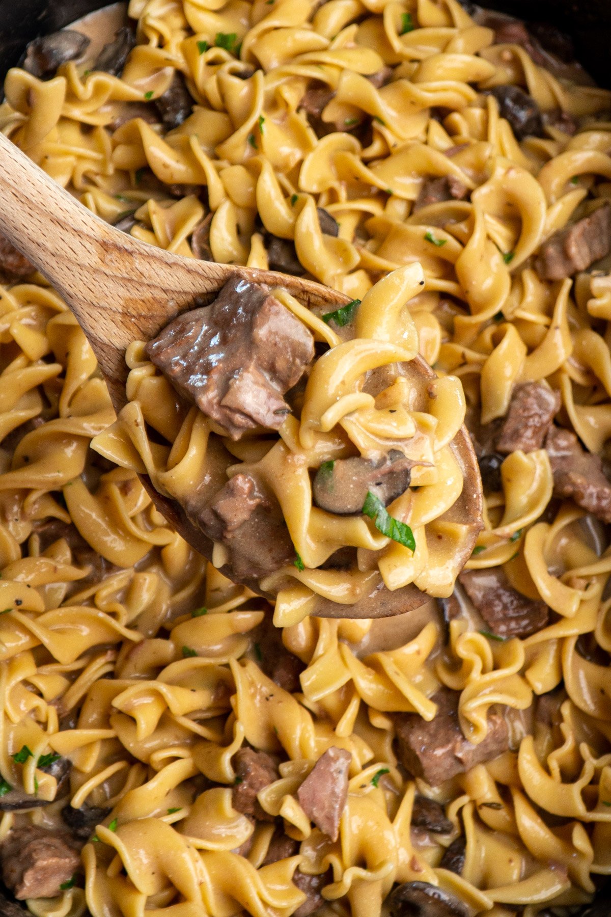 Beef stroganoff on a wooden spoon over a slow cooker.