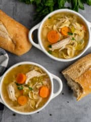 Overhead look at Crock Pot chicken noodle soup in two white bowls with bread on the side.