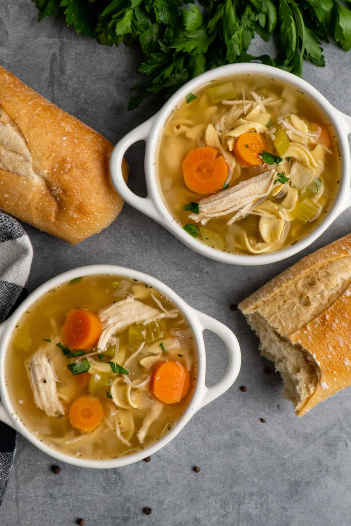 Overhead look at Crock Pot chicken noodle soup in two white bowls with bread on the side.