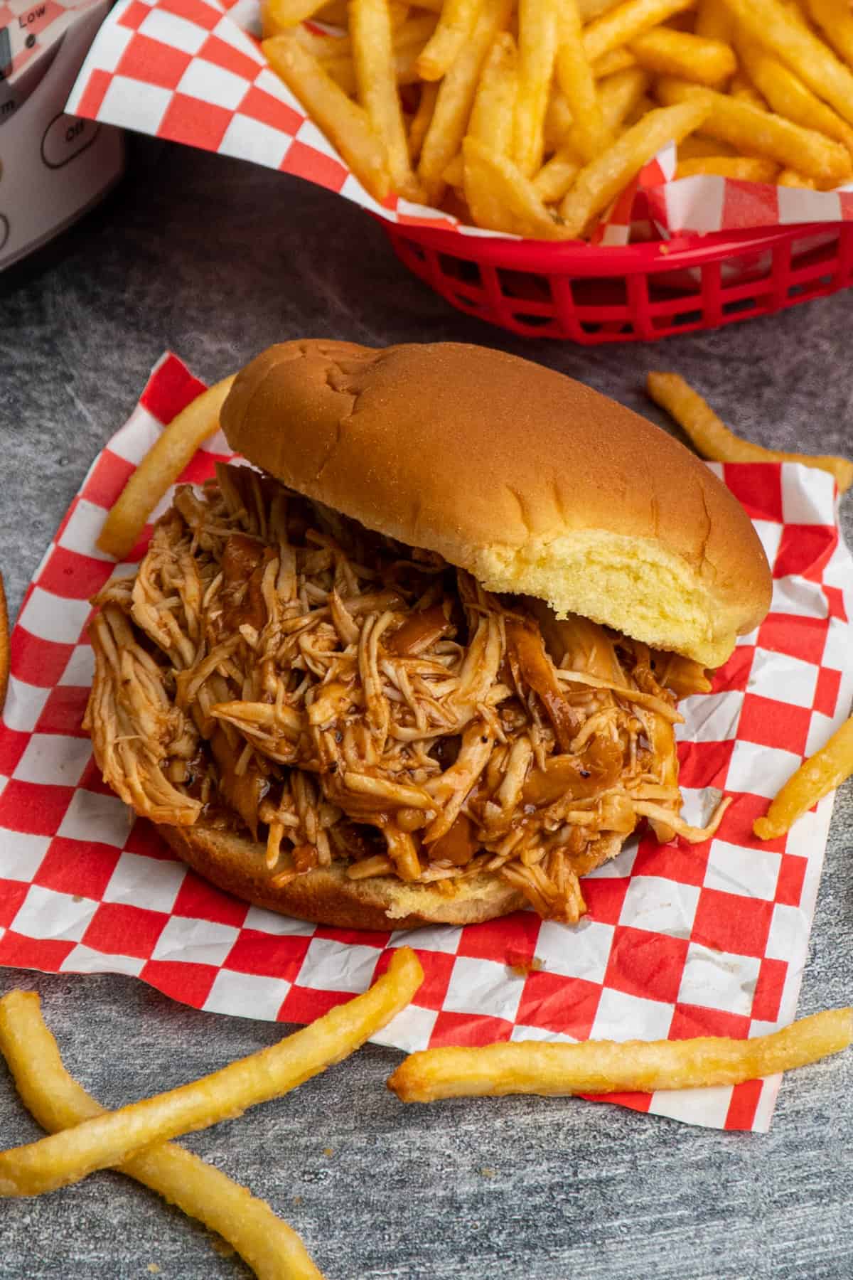 Crock Pot Dr. Pepper shredded chicken on a bun with fries in the background.