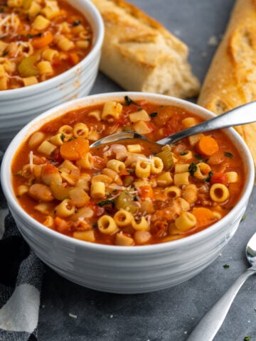 Close up of Crock-Pot pasta fagioli in a white bowl with bread in the background.