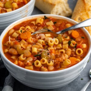 Close up of Crock-Pot pasta fagioli in a white bowl with bread in the background.
