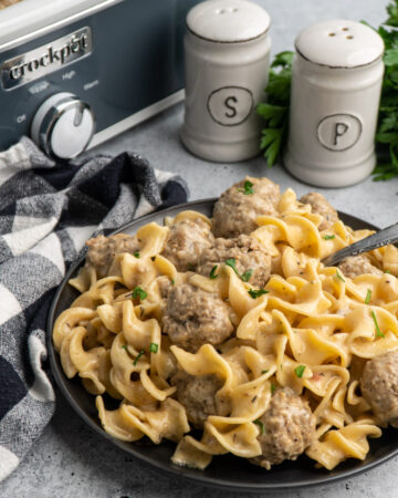 Crock-Pot Swedish meatballs on a black plate with salt and pepper in the background.