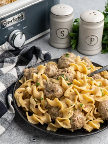 Crock-Pot Swedish meatballs on a black plate with salt and pepper in the background.