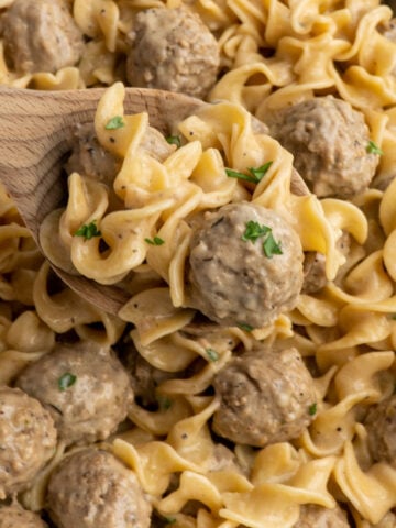 Swedish meatballs on a wooden spoon over a Crock-Pot.