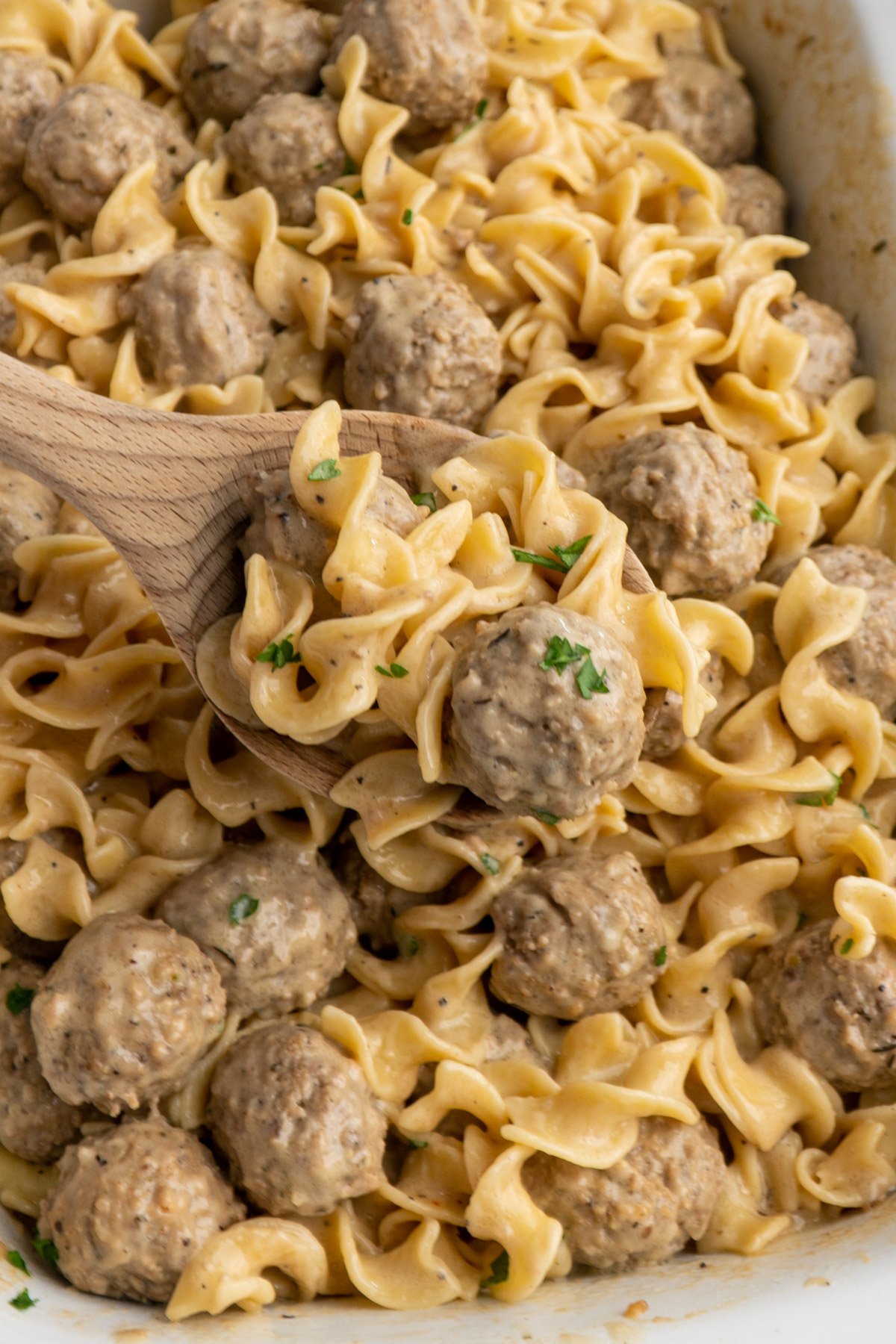 Close up of Swedish meatballs on a wooden spoon over a Crock-Pot.