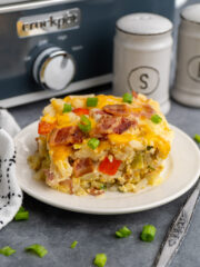 Close up of breakfast casserole on a white plate with a Crock-Pot in the background.