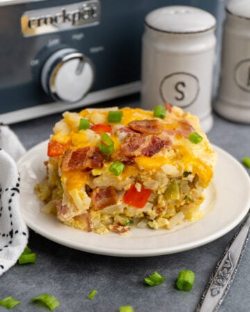 Close up of breakfast casserole on a white plate with a Crock-Pot in the background.
