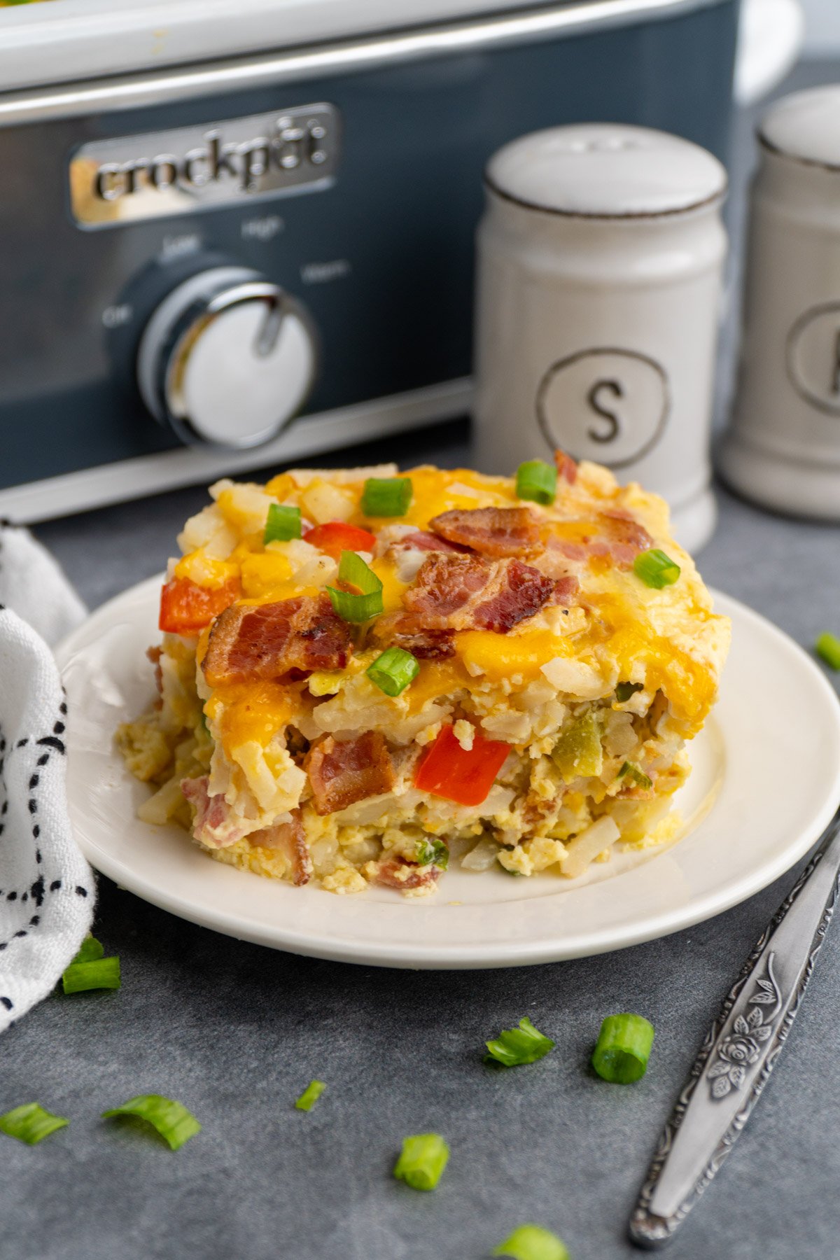 Close up of breakfast casserole on a white plate with a Crock-Pot in the background.