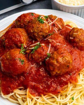 Homemade Crockpot meatballs on a plate of spaghetti and garnished with fresh parsley.