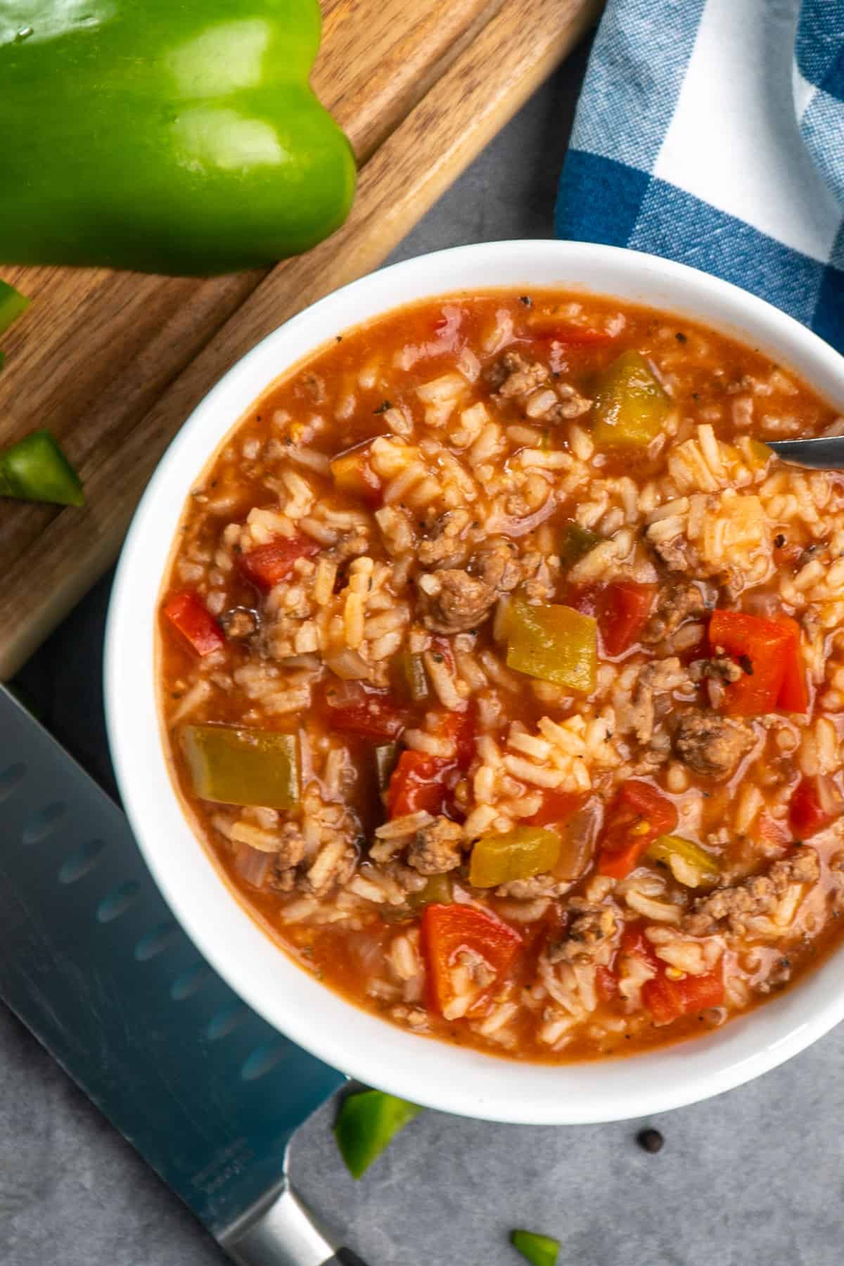 Overhead look at crock pot stuffed pepper soup in a white bowl with a green pepper in the back ground.