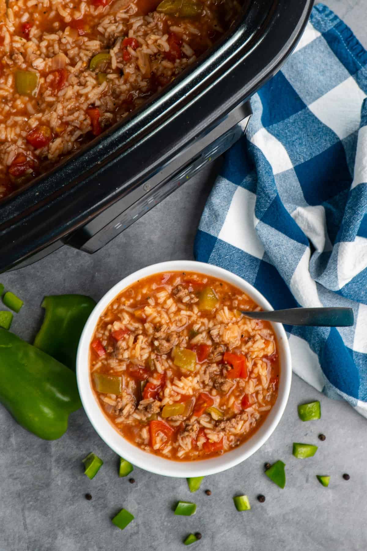 Overhead look at stuffed pepper soup in a slow cooker and a white bowl.