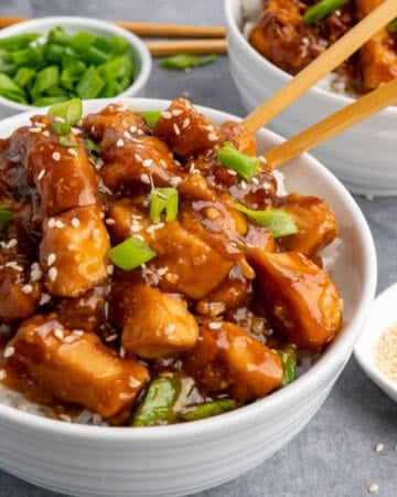 Close up of slow cooker general Tso chicken over rice in a white bowl with chopstick in it.