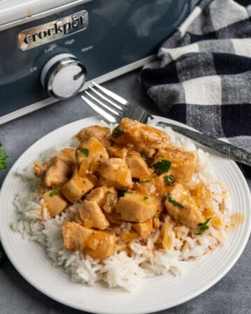 Close up of slow cooker honey bourbon chicken over rice on a white plate.