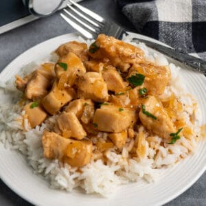 Close up of slow cooker honey bourbon chicken over rice on a white plate.