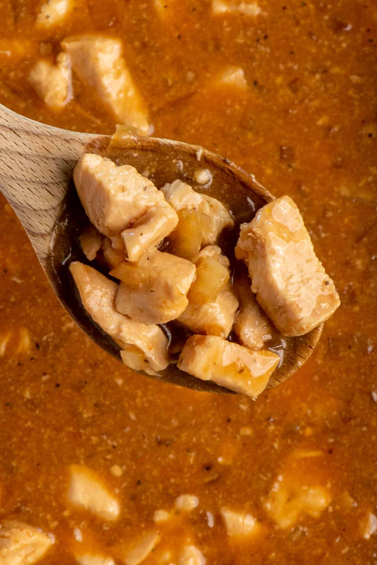 Close up of honey bourbon chicken on a wooden spoon over a Crockpot.