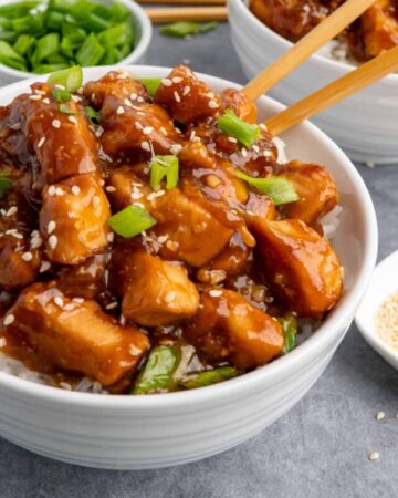 Close up of slow cooker general Tso chicken over rice in a white bowl with chopstick in it.