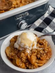 Crock pot apple crisp in a white bowl with ice cream on top.