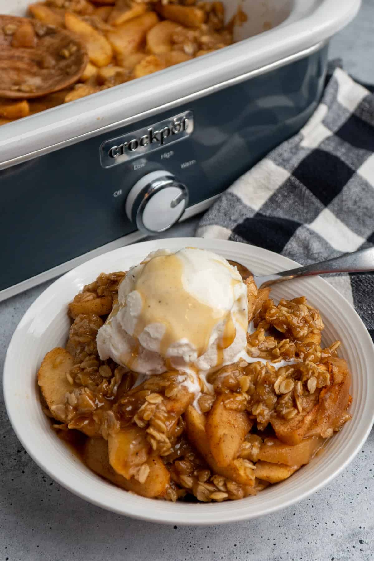 Crock pot apple crisp in a white bowl with ice cream on top.