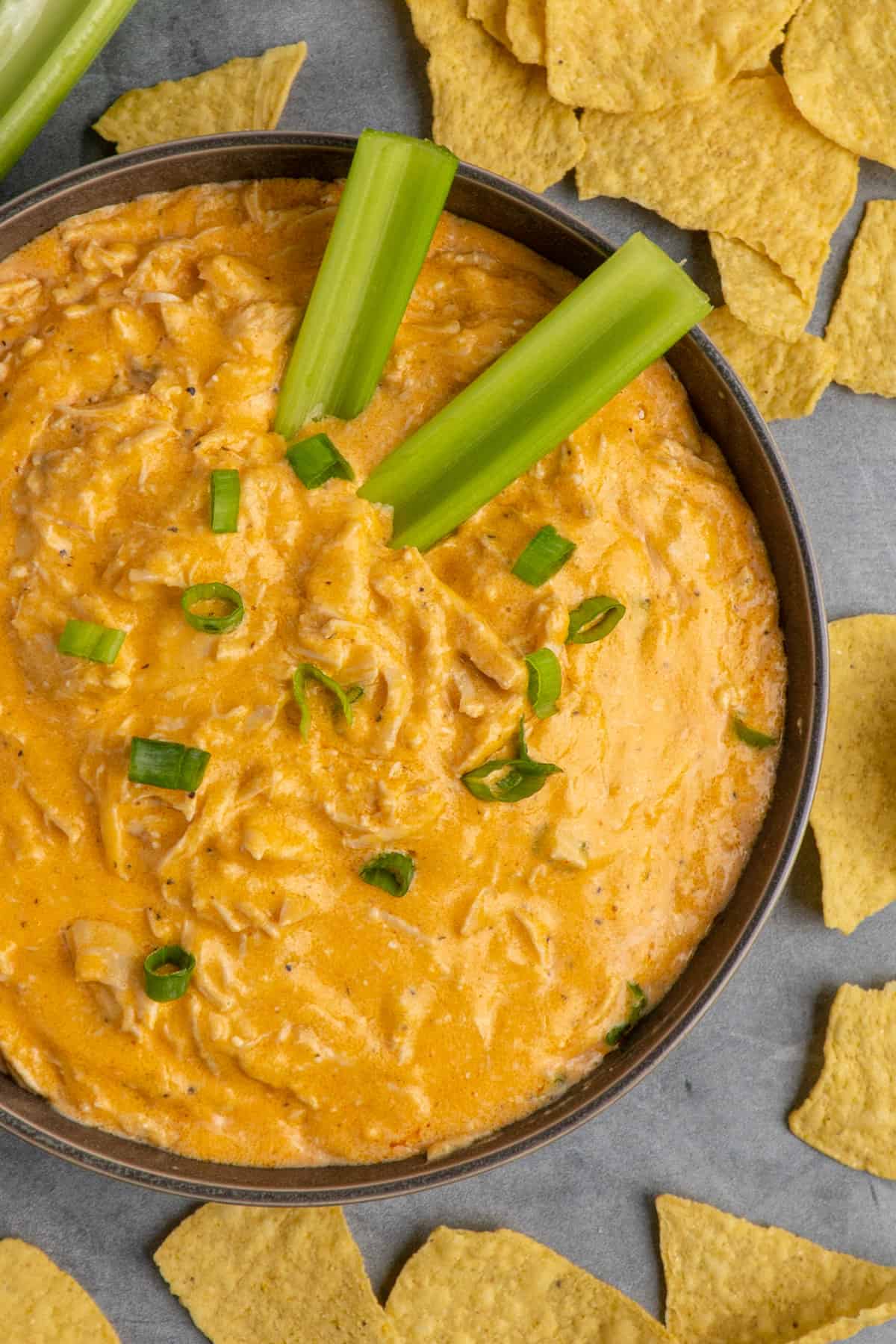 Overhead look at Crock Pot buffalo chicken dip in a grey bowl surrounded by tortilla chips.