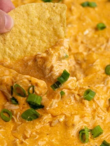 Close up of a tortilla chip being dipped in to Crock Pot buffalo chicken dip.